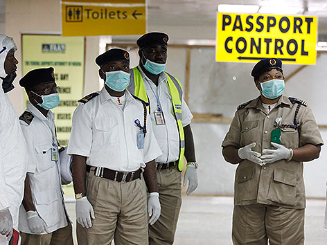 © APA/AP/Sunday Alamba Maskierte Gesundheitsbeauftragte und Polizei am Flughafen in Lagos