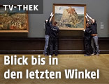 Personen h&auml;ngen Gem&auml;lde an die WandFrau legt einen Plastikkopf auf ein Regal