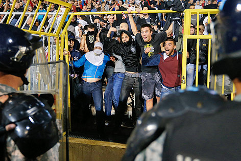Fußballfans blicken durch eine geöffnete Absperrung auf Polizisten