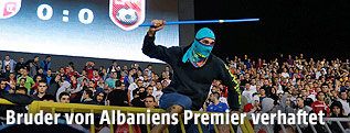 Ein vermummter Mann mit Stange &uuml;berspringt eine Stadionabsperrung