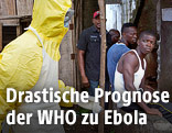Ein Mediziner in Schutzanzug neben liberianischen Männern