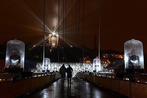 © Ville de Lyon - M. Chaulet Zwei Personen gehen über eine Brücke, in der der Ferne beleuchtete Gebäude