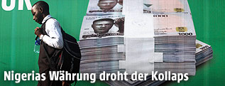 Ein Mann geht an einem Plakat mit nigerianischen Naira-Banknoten vorbei