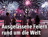 Menschen blicken aufs Meer hinaus auf ein Feuerwerk