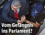 Nikos Michaloliakos (Goldene Morgenröte) in Handschellen neben einem Polizisten
