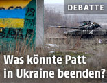 Panzer und Holzhütte mit aufgemalter ukrainischen Flagge