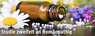 Geöffnete Flasche mit homöopathischen Globuli neben Blumen