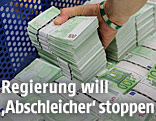 Eine Hand greift nach einem Stapel 100-Euro-Scheine