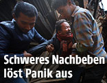 Zwei Männer tragen einen weinenden Mann aus einem zerstörten Haus