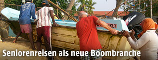 Ein Tourist schiebt auf Sri Lanka mit Einheimischen ein Boot aus dem Wasser