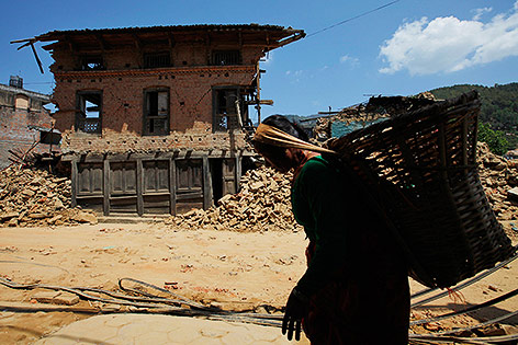 © AP/Niranjan Shrestha Frau trägt einen Korb vor einem zerstörten Haus