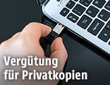Eine Hand steckt einen USB-Stick an einen Laptop an