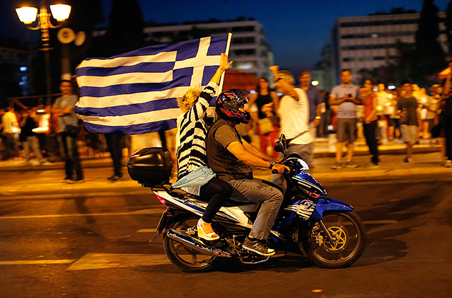 © APA/AP/Emilio Morenatti Frau und Mann fahren auf einem Motorrad und schwenken die griechische Fahne