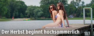 Junge Frauen sitzen auf einem Steg bei einem See