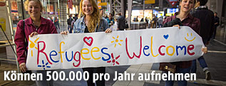 Menschen halten ein Plakat mit der Aufschrift "Refugees Welcome"