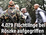 Ein Polizist und ein Soldat beobachten Flüchtlinge