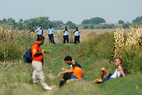 Kroatische Polizisten beobachten Flüchtlinge auf einem Feld