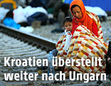 Mutter mit Kind sitzt in Decken eingehüllt auf den Bahngleisen auf dem Bahnhof Tovarnik, Kroatien