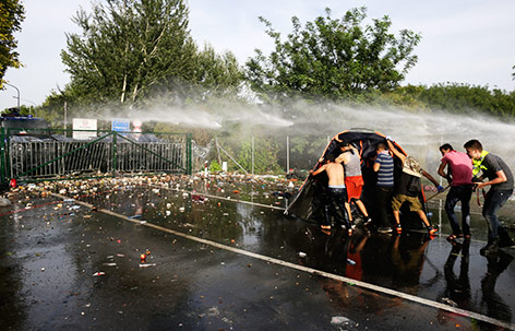 © Reuters/Stoyan Nenov Flüchtlinge suchen hinter einem Zelt Schutz vor der ungarischen Polizei und deren Einsatz von Wasserwerfern