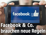 Mann h&auml;lt Handy mit Facebook-Logo