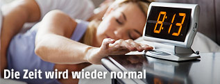Frau im Bett drückt Snooze auf Wecker
