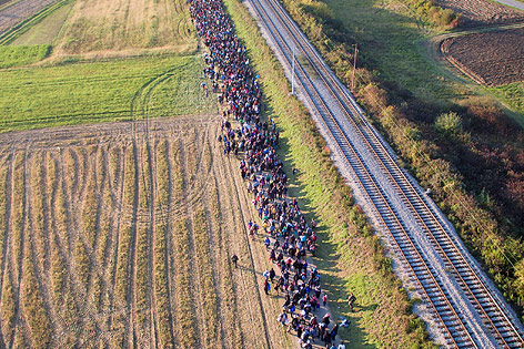 Lange Schlange von Flüchtlingen, die an Bahnschienen entlangmarschieren
