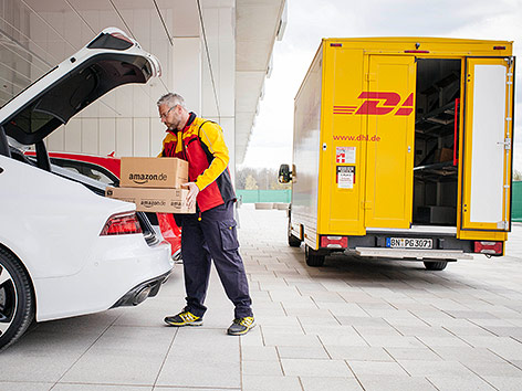 © DHL Zusteller mit einem Paket bei einem Kofferraum
