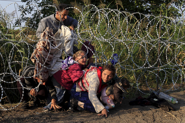 © Reuters/Bernadett Szabo Flüchtlinge überwinden einen Grenzzaun
