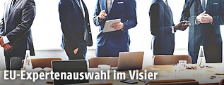M&auml;nner in Anz&uuml;gen sprechen neben einem Sitzungstisch miteinander