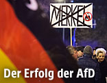 Demonstranten halten ein Schild in welchem der Schriftzug Merkel durchgestrichen ist