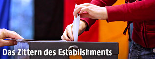 Person steckt Stimmzettel in eine Wahlurne