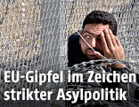 Mann sitzt vor einem Zaun und Stacheldraht