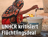 Ein weiblicher Fl&uuml;chtling f&uuml;llt Wasser in einen K&uuml;bel mit UNHCR-Zeichen