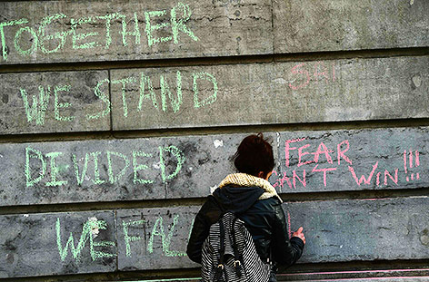 © APA/AFP/Emmanuel Dunand Frau schreibt "Together we stand, devided we fall" sowie "Fear can't win" auf eine Wand