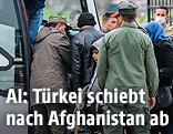 Flüchtlinge besteigen neben türkischen Sicherheitsbeamten einen Bus