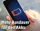 Frau hält Handy mit leerem Akku in der Hand