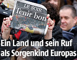 Eine Person hält bei einer Schweigeminute in Brüssel eine Zeitung mit der Schlagzeile "Tenir bon" in die Höhe