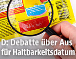 Jemand schaut mit einer Lupe auf das Haltbarkeitsdatum