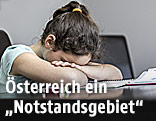 Mädchen senkt Kopf auf Arme am Schreibtisch