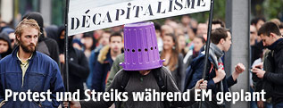 Demonstrant mit K&uuml;bel am Kopf und Transparent in der Hand