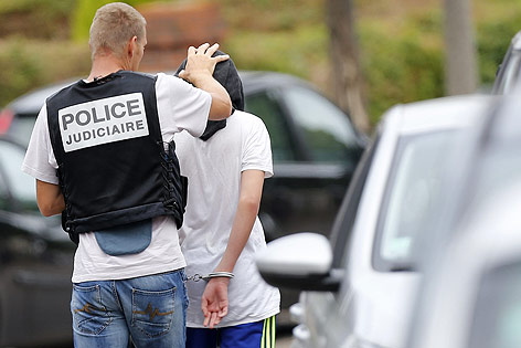 Ein französischer Polizist führt einen Mann mit Kapuze und Handschellen ab