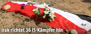 Blumen und eine Fahne erinnern an ein Massengrab