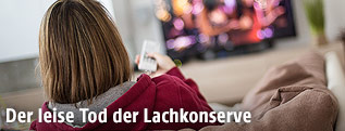 Frau sitzt mit Fernbedienung vor Fernseher