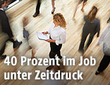 Eine Frau liest Unterlagen neben vorbeihastenden Personen