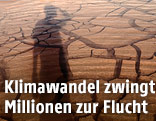 Schatten eines Menschen auf einem &uuml;berschwemmten, ausgetrockneten Boden