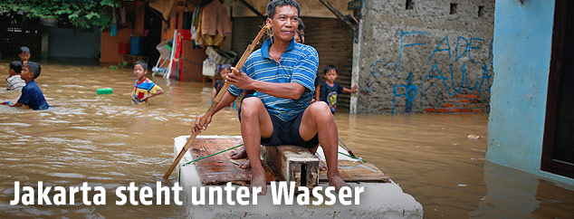 Ein Mann fährt mit einem Floß durch das überschwemmte Jakarta