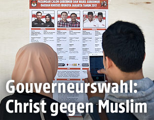 Eine Frau und ein Mann vor einem Infozettel mit den Kandidaten der indonesischen Gouverneurswahl