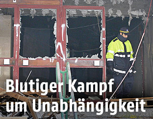 Ein Polizist neben einer von einer Bombenexplosion zerstörten Tür