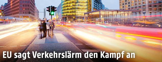 Autolichter auf einer stark frequentierten Straße und Fußgänger auf einer Verkehrsinsel