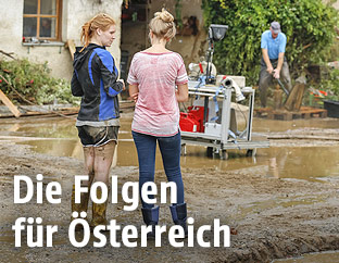 Zwei Frauen stehen vor einem Haus im Schlamm